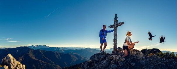 Pärchen im Sommer mit Bergdohlen am Gipfelkreuz der Hörndlwand in Ruhpolding