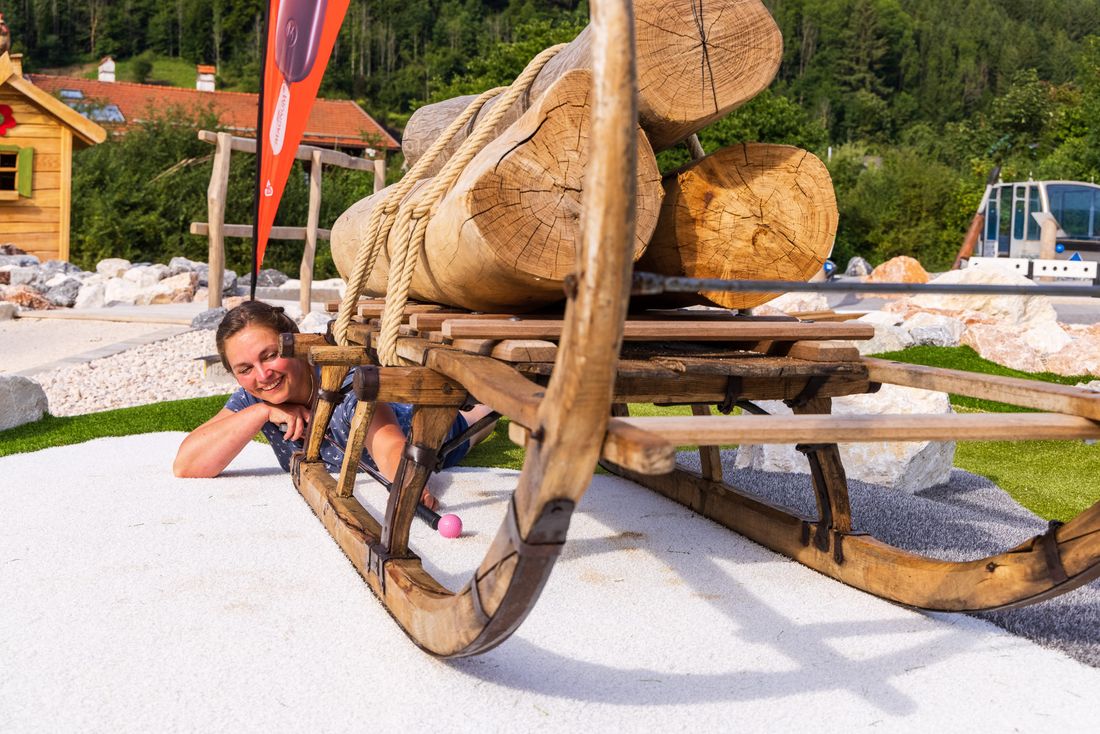 Frau posiert an einem Holzschlitten auf der Minigolf Anlage